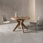 Imagen de la Mesa Roma de melamina con base de madera en forma de cruz y tapa redonda. aparece cerrada con dos sillas.